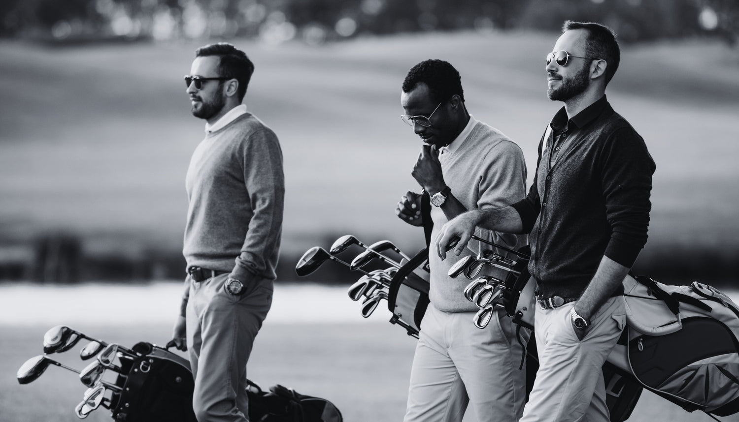 Three stylish men walking walking on golf course carrying golf clubs 