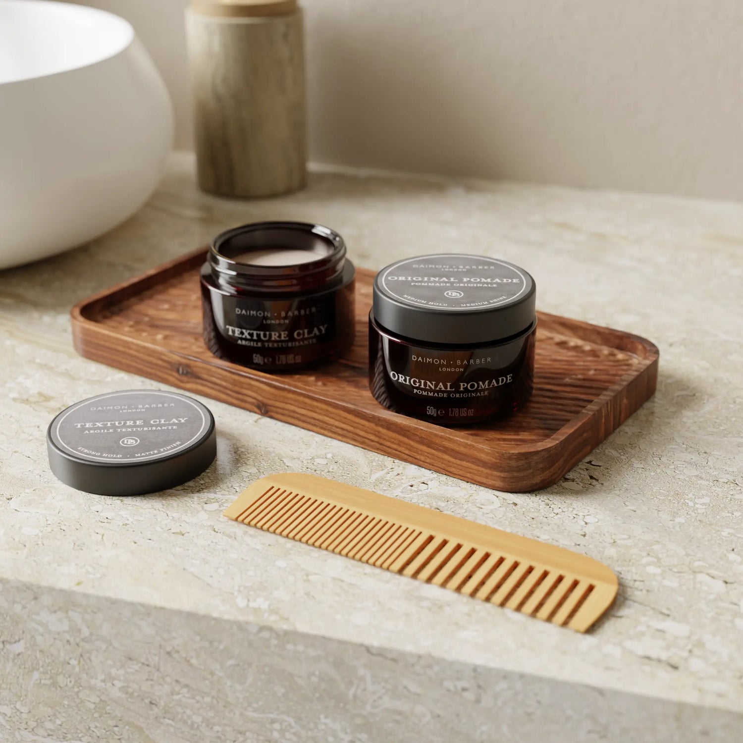 Open pot of Texture Clay and Original Pomade next to a bathroom sink with a comb for men’s hair styling.