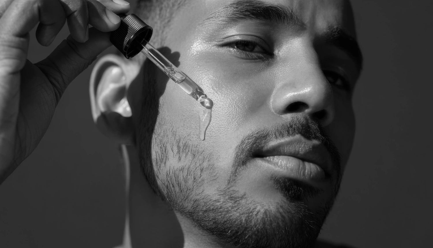 Man applying face serum pipette to face in black and white