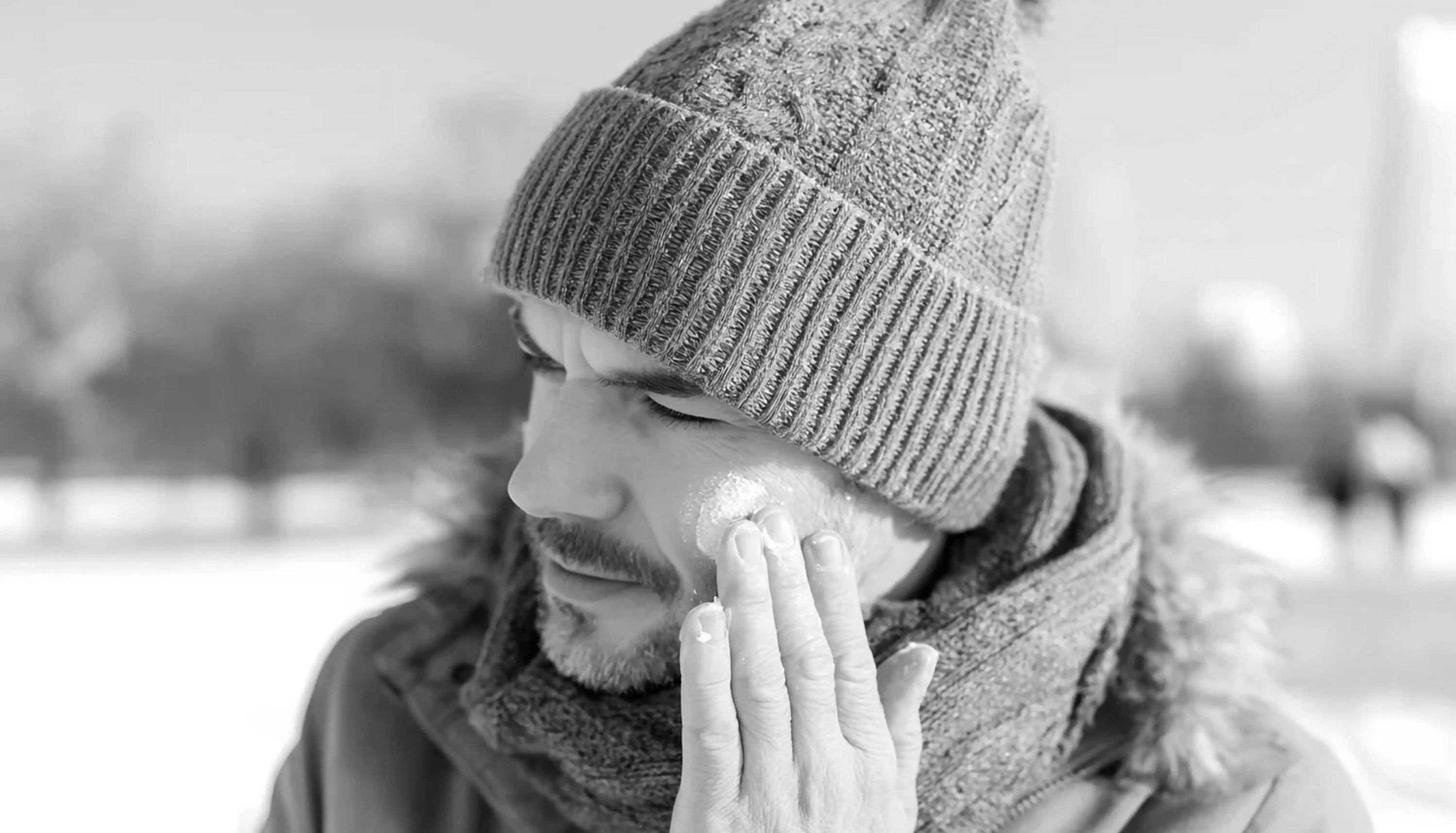Man applying moisturiser outdoors in winter clothing in black and white