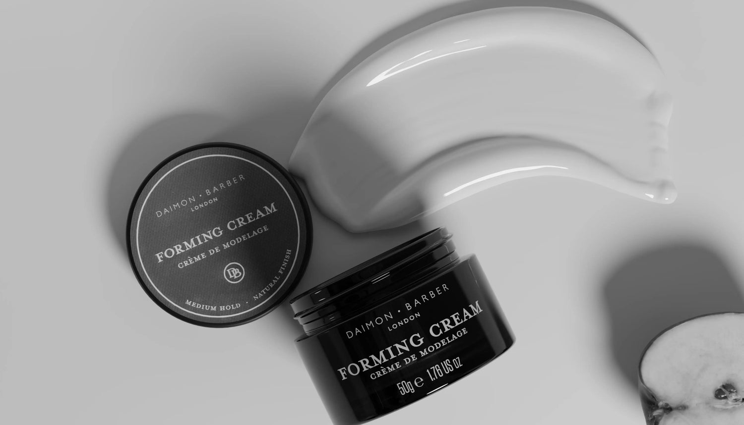 Hair cream texture with an opening pot of daimon barber forming cream with lid and apple in black and white