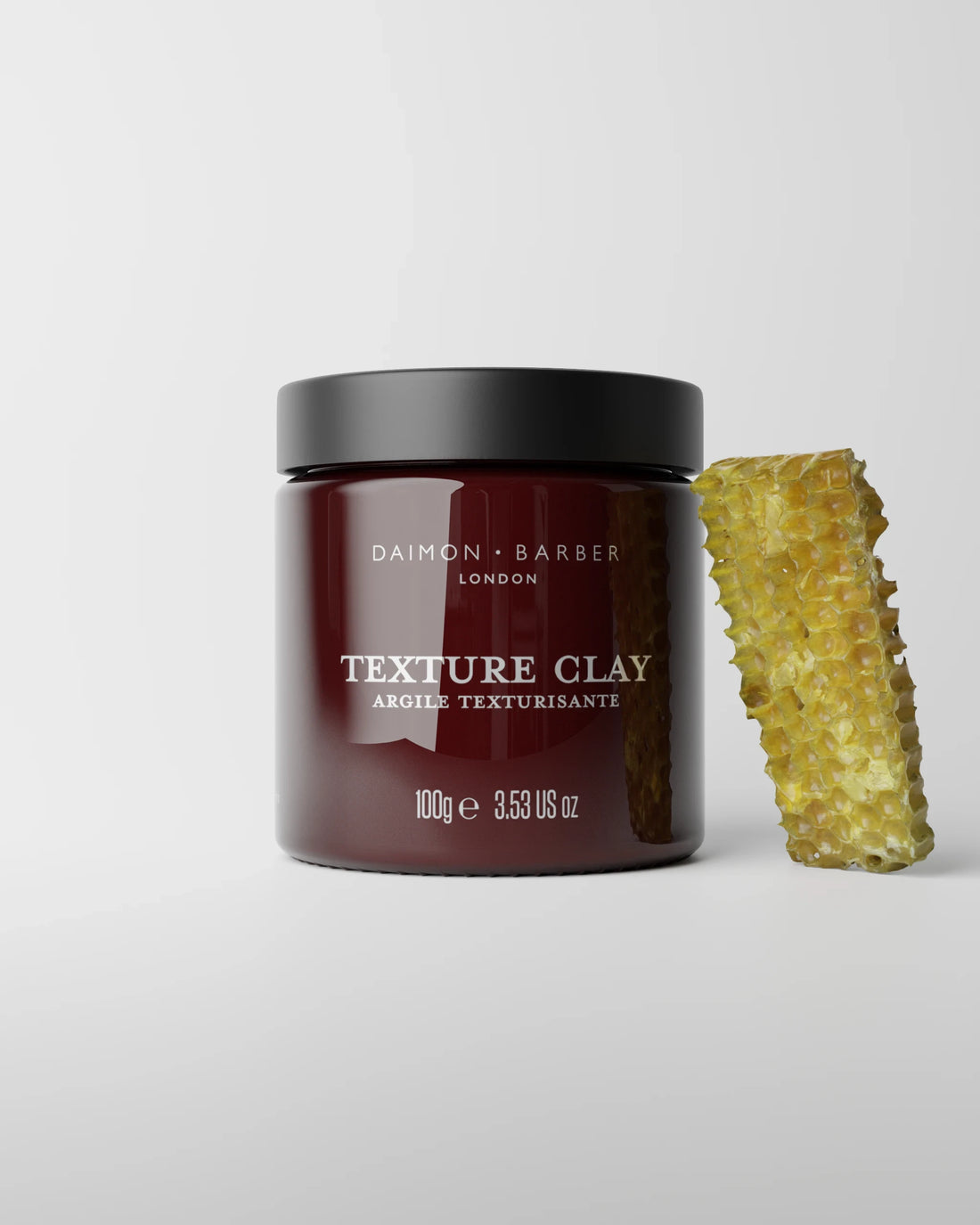 Jar of Daimon Barber Texture Clay 100g with a honeycomb on a light gray background