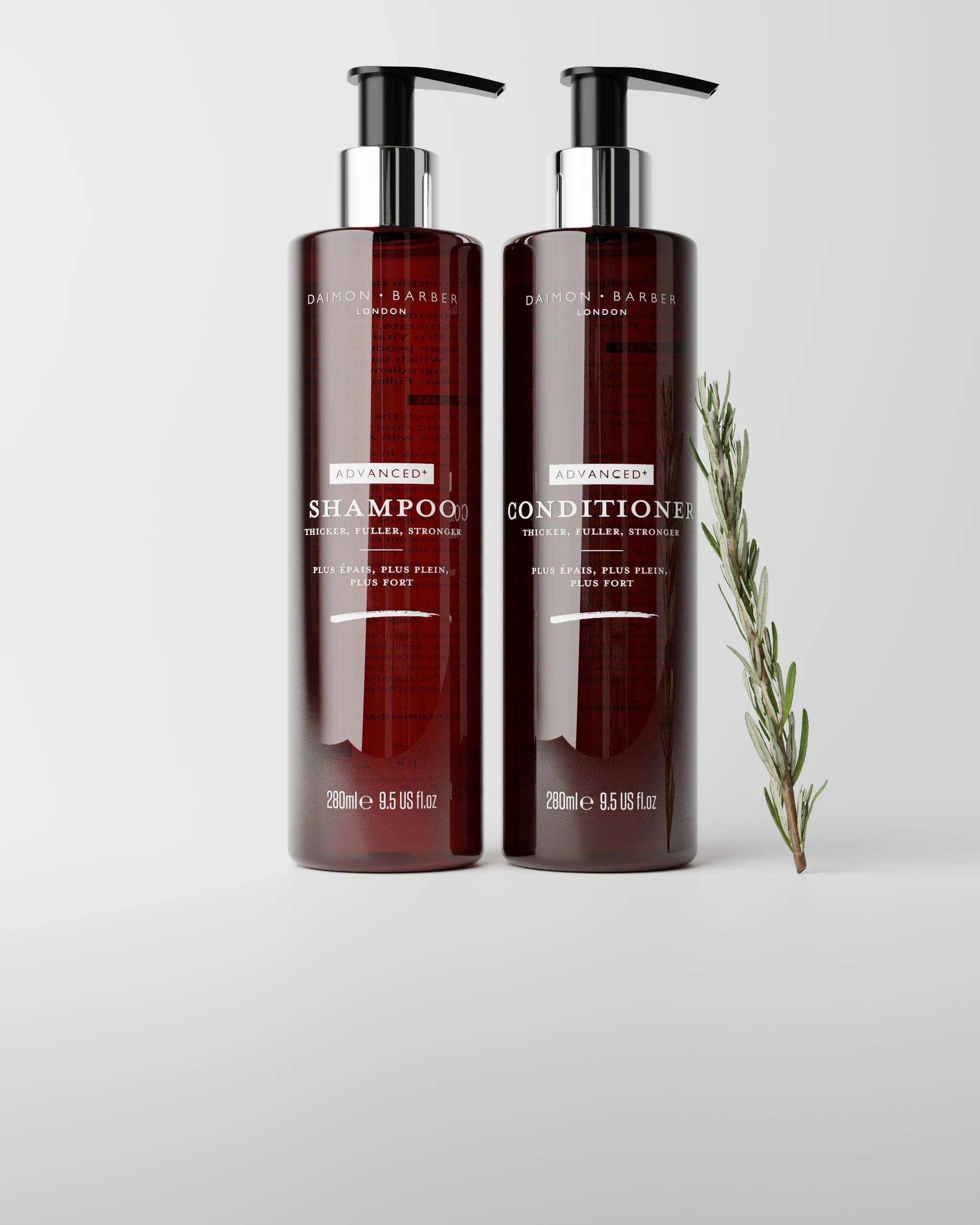 Two bottles of shampoo and conditioner with rosemary on a grey background.