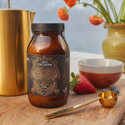 Bottle of True Collagen on a wooden table with a gold measuring spoon and strawberries.