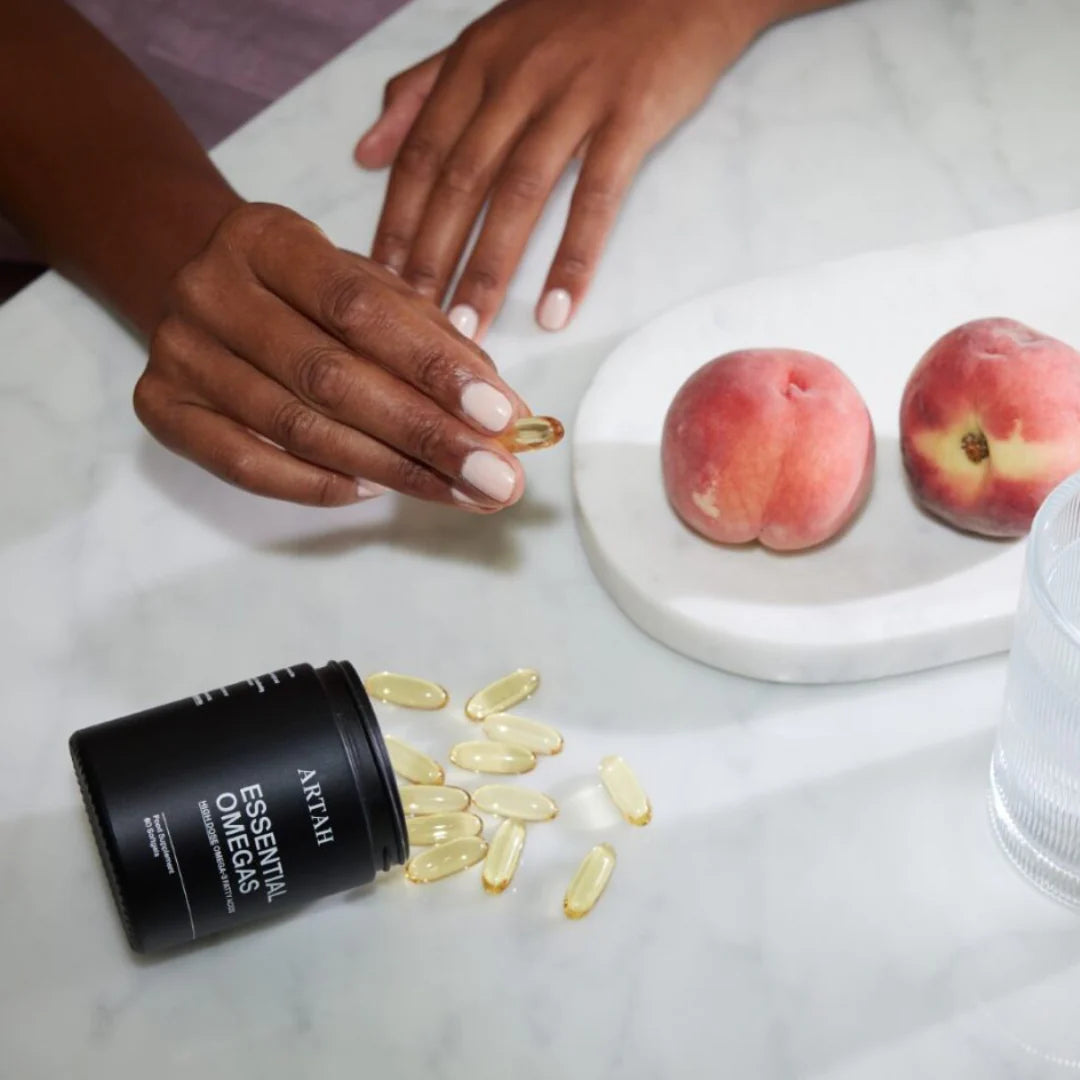 Person holding a supplement capsule with a bottle of supplements and peaches on a table.